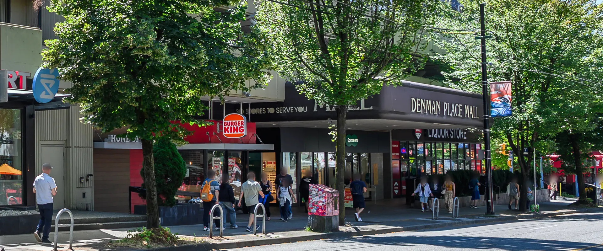 The Denman Place Mall entrance and sign on Denman Street on a sunny day, with Burger King, Specsavers and the liquor store under the trees